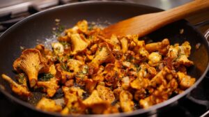 Chanterelle mushrooms being sautéed with fresh herbs and garlic in a pan