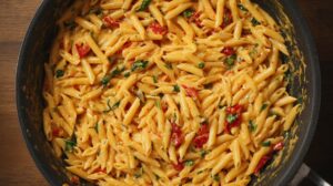 Close-up of penne pasta mixed with creamy sauce, herbs, and bits of sun-dried tomatoes