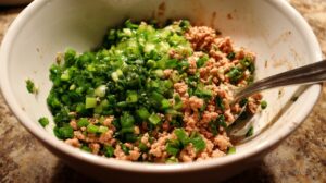 Close-up of a bowl with ground meat and chopped green onions being mixed for wonton filling.