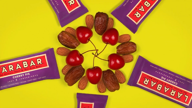 Larabars Cherry Pie bars arranged with cherries, almonds, and dates on a yellow background