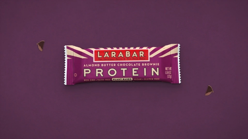 Larabars Almond Butter Chocolate Brownie Protein bar on a purple background with small chocolate pieces beside it