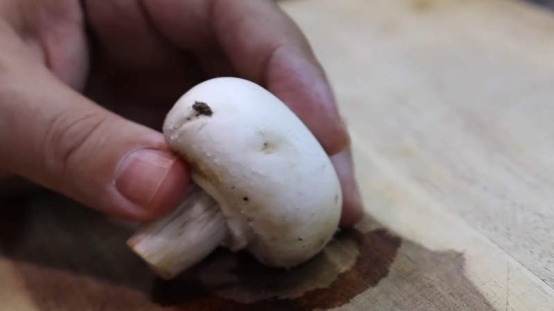 A mushroom is wiped clean by hand without soaking to avoid waterlogging