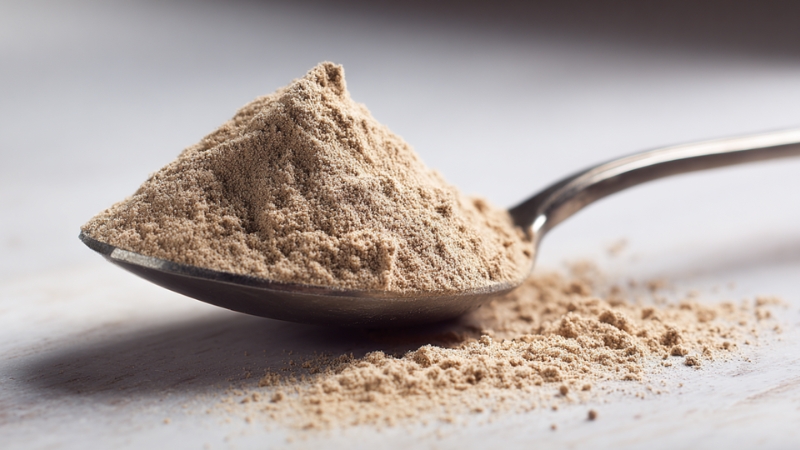 Spoon filled with fine mushroom powder scattered on a white surface