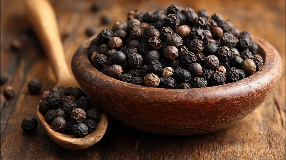 Bowl of whole black peppercorns on a wooden surface